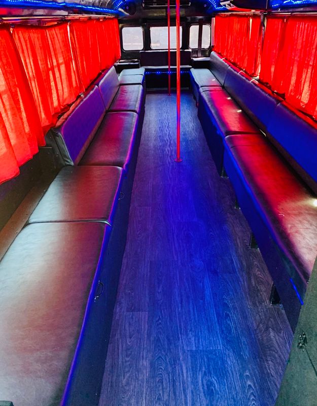 The interior of a party bus with red curtains, leather bench seating, a dance pole and blue LED lighting.
